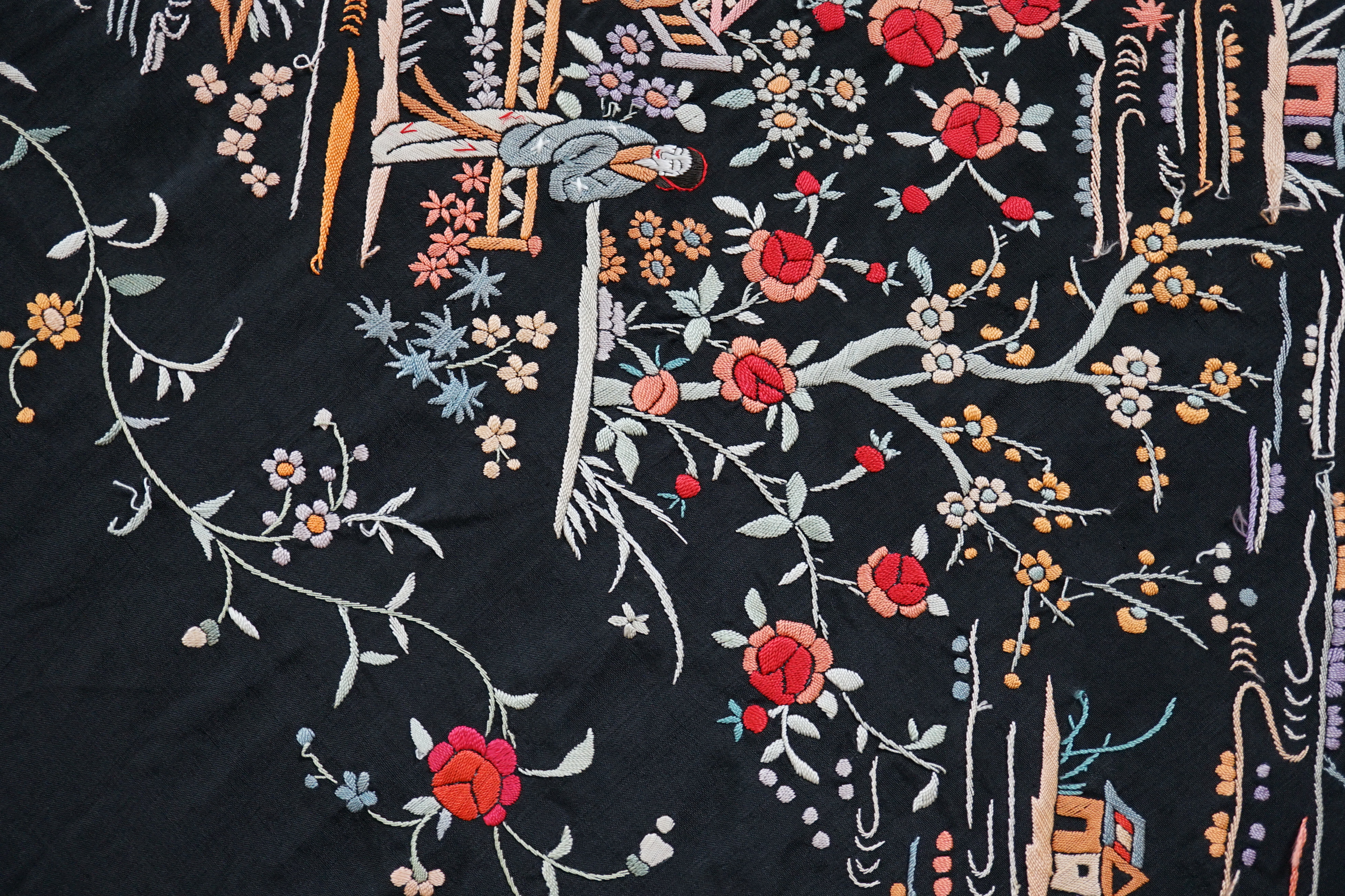 An early 20th century Chinese black silk shawl, with all over coloured floral embroidery, embroidered with multi-coloured silks and a long silk fringe, unusually the four corners are embroidered with a figurative pagoda